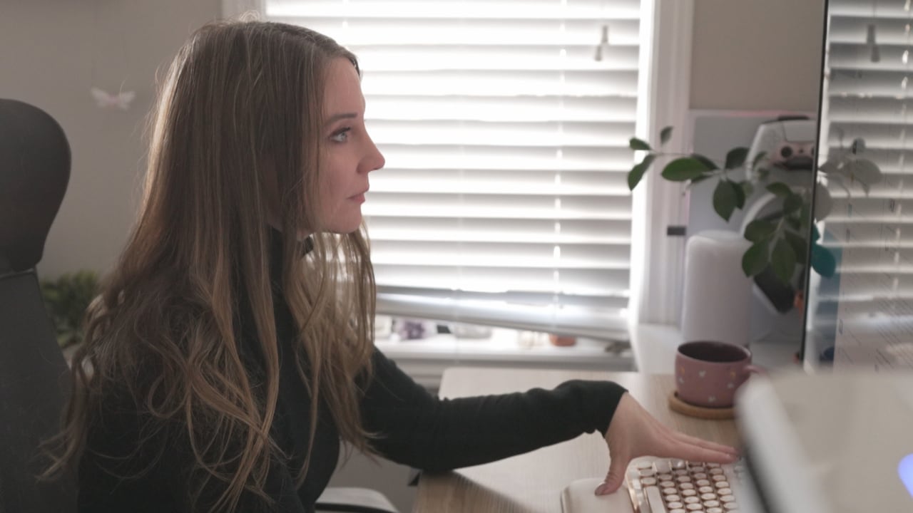 A profile-shot of a woman sitting at a desk, looking at a monitor screen.