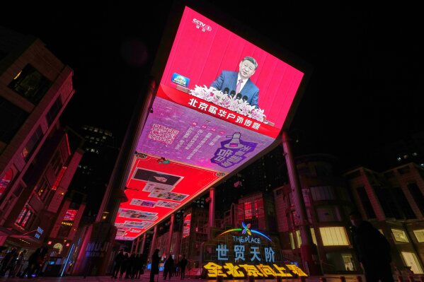 People gather underneath a large screen at a shopping mall showing CCTV broadcasting Chinese President Xi Jinping, also general secretary of the Communist Party of China Central Committee and chairman of the Central Military Commission as he speaks at the New Year gathering held by the National Committee of the Chinese People's Political Consultative Conference (CPPCC), in Beijing, Wednesday, Dec. 31, 2025. (AP Photo/Andy Wong)