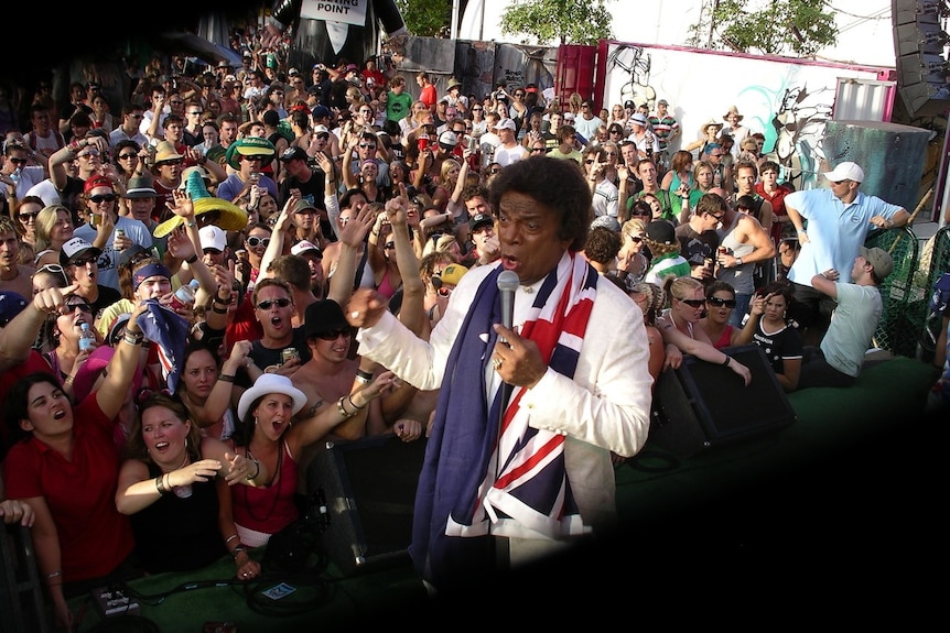 Kamahl singing to a crowd draped in an Australian flag