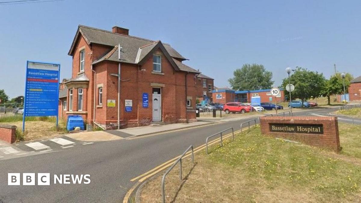 Google streetview image of the entrance to Bassetlaw hospital, showing a detached Victorian red brick house next to a name plate, with cars parked in the background