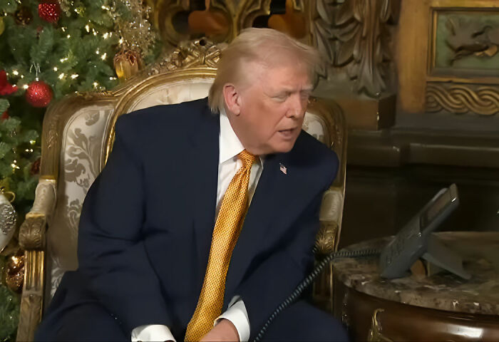 Donald Trump sitting in an ornate chair near a decorated Christmas tree, speaking on a phone about bad Santa comments.