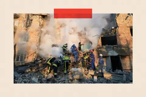Getty Images Firefighters douse flames at a residential building while rescuers search the rubble for victims after a Russian ballistic missile strike in Kyiv, Ukraine
