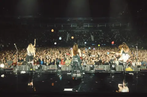 Jono White Haim pictured on stage. They are shot from behind in order to show the vast audience, who are throwing multi-coloured beach balls into the air