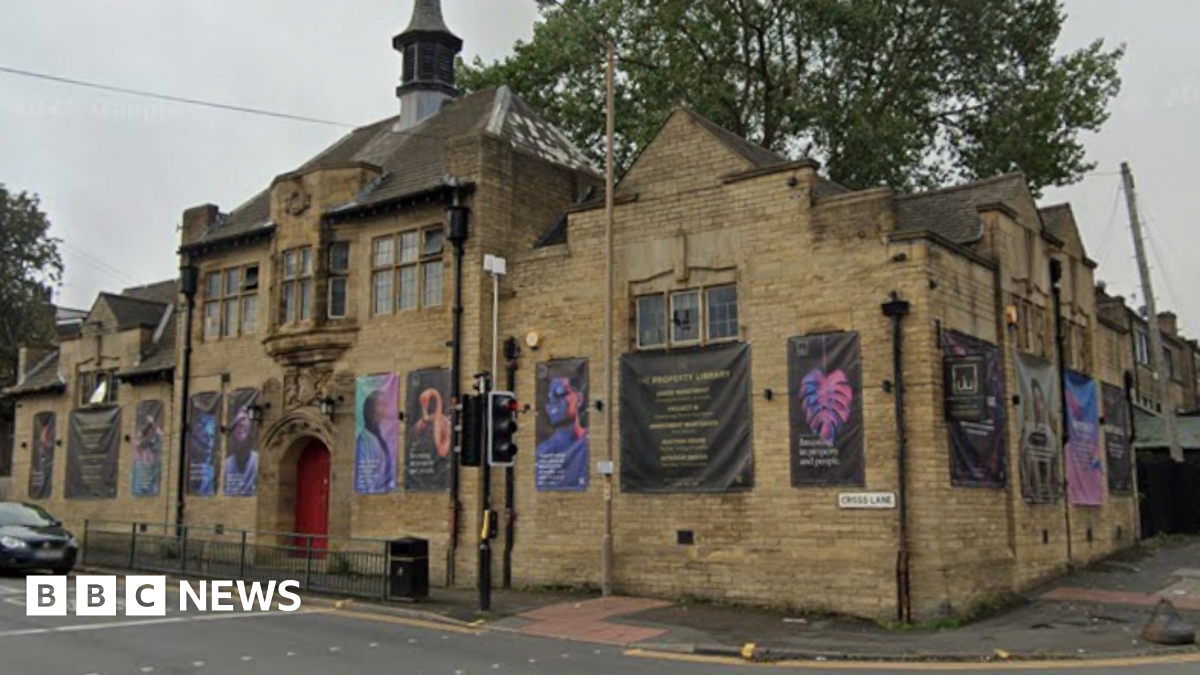 A photo of a beige stone building on a street corner. Along its walls are many black, white and blue advertising banners.