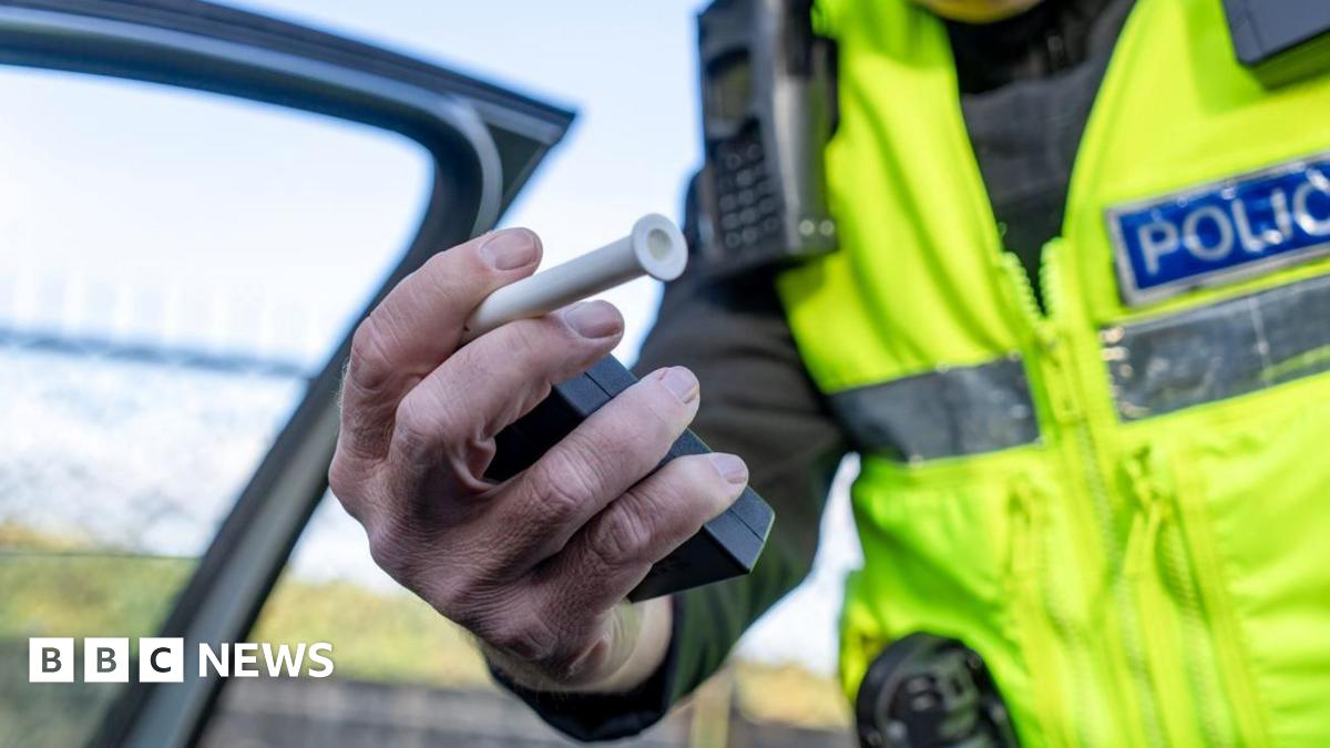 A man in an yellow reflective jacket holding out a black box with a white tube coming out of it