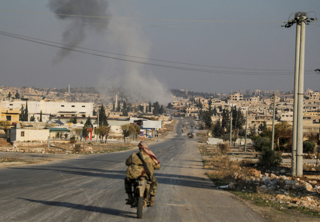 Smoke rises as a member of the rebels led by the Islamist militant group Hayat Tahrir al-Sham drives on a motorbike in al-...