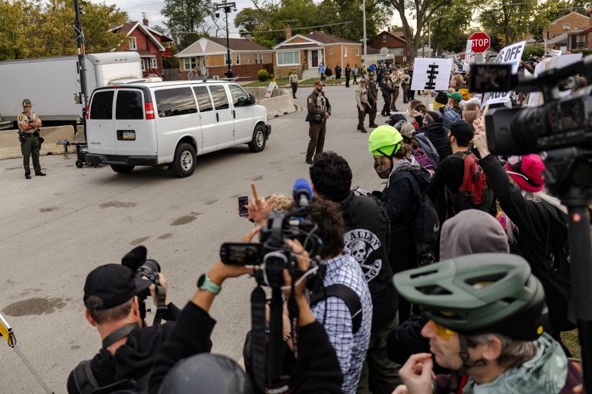 A transportation van leaves the Broadview ICE facility as protesters stand behind barricades in Broadview, Illinois, on October 10.