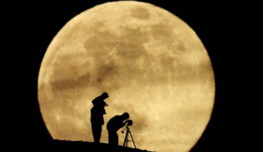 A couple and their daughter use a telescope to observe the last supermoon of 2025, known as the Cold Moon, in Aguimes