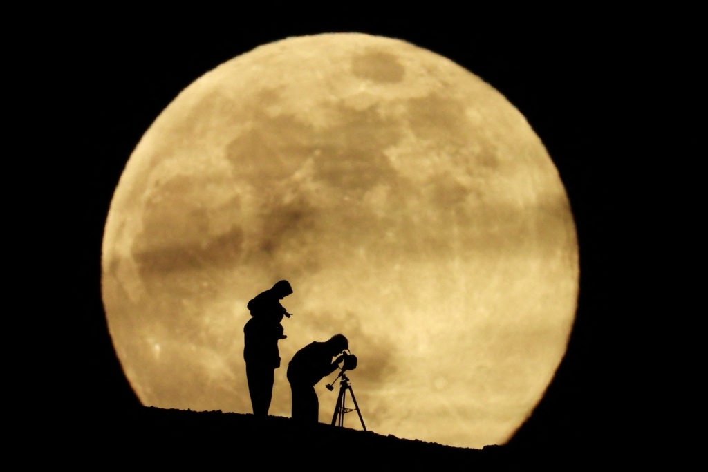 A couple and their daughter use a telescope to observe the last supermoon of 2025, known as the Cold Moon, in Aguimes