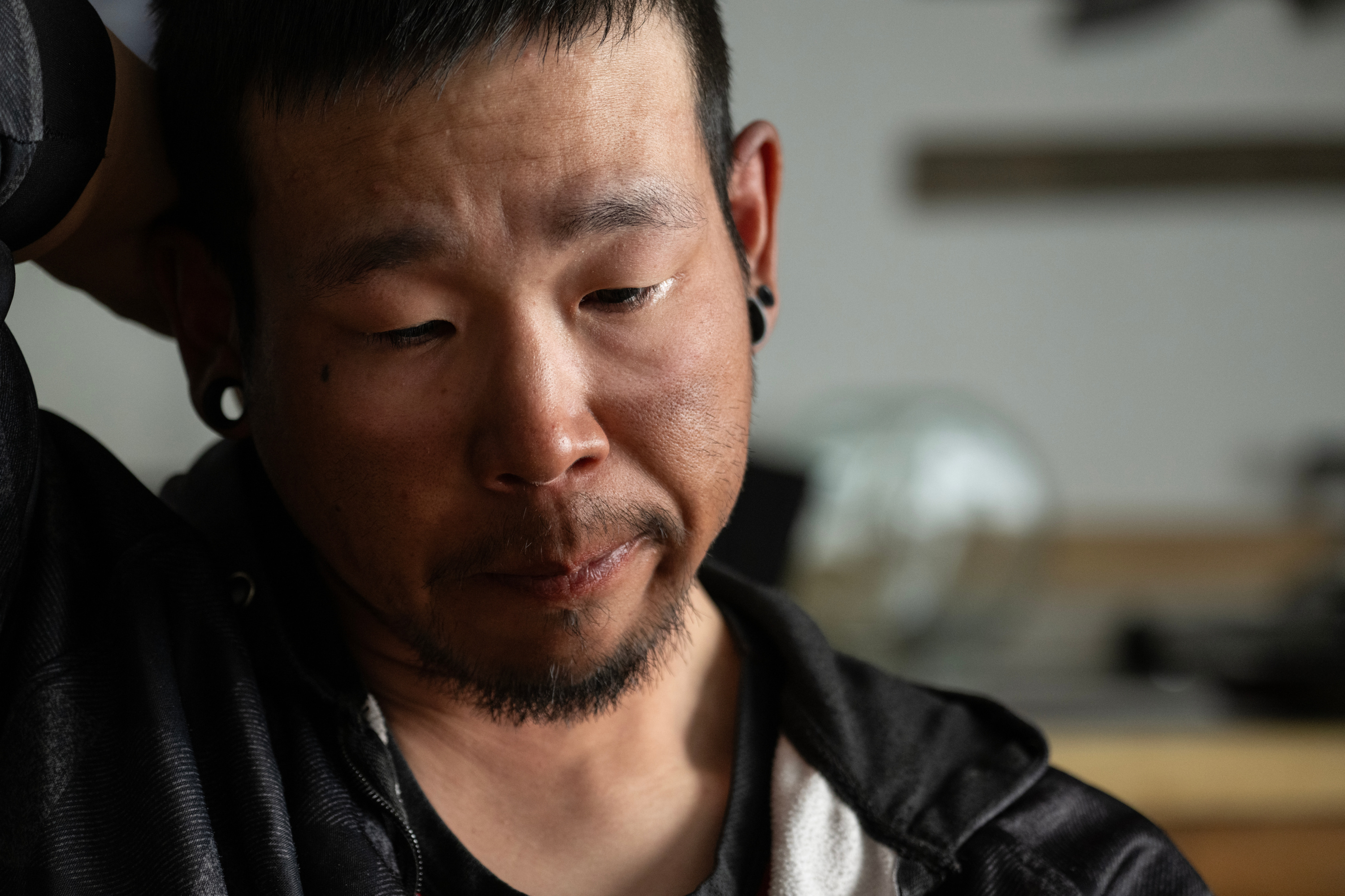 A man with a goatee and gages holds the back of his head and cries.