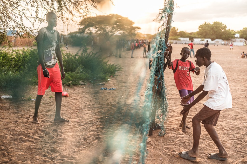 Several boys hang out around a tattered net while other boys play soccer in the background.