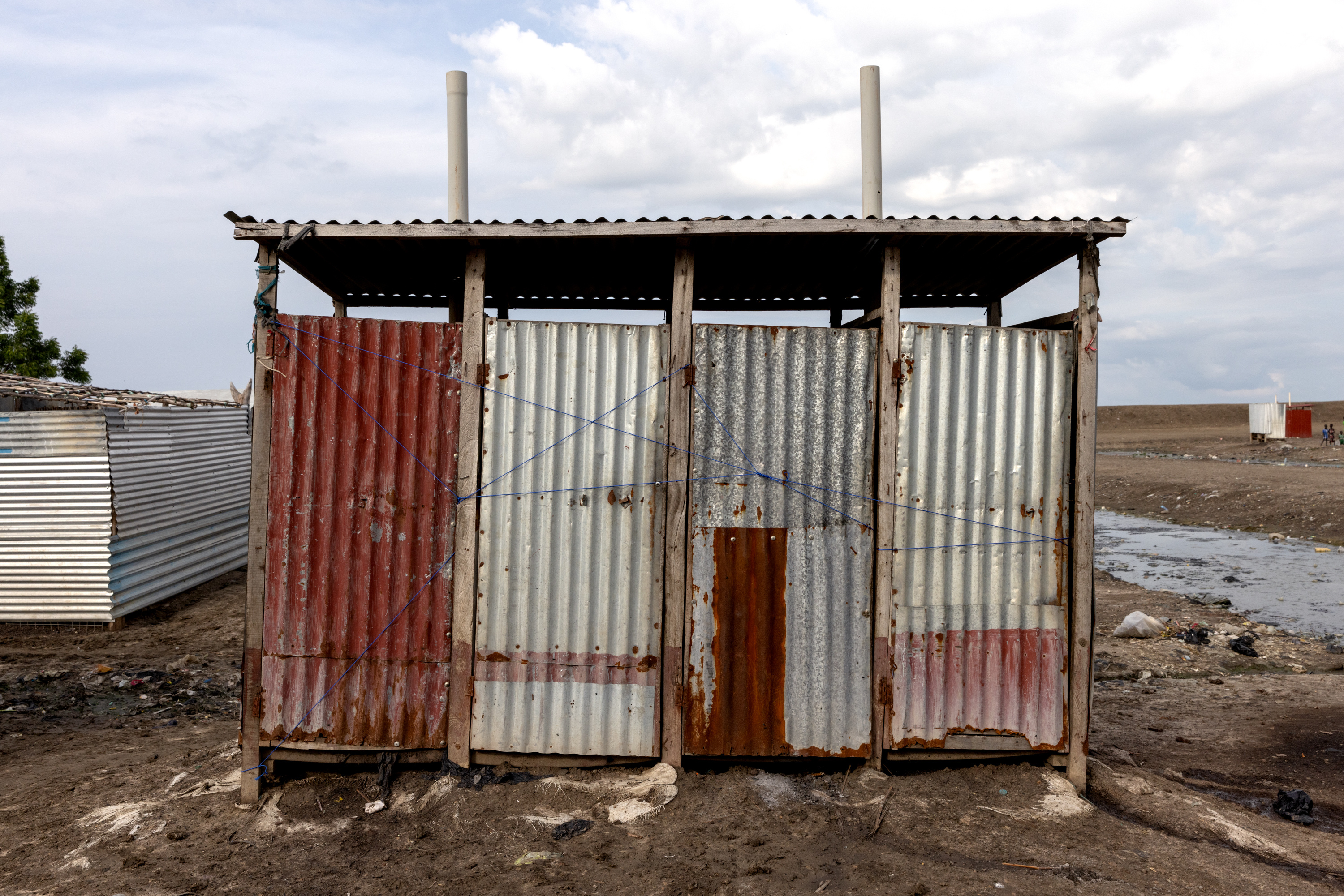 A latrine in the midst of a refugee camp with doors that have been tied shut with string.