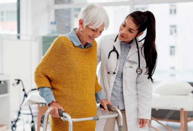 Doctor and elderly woman using a walker for support.