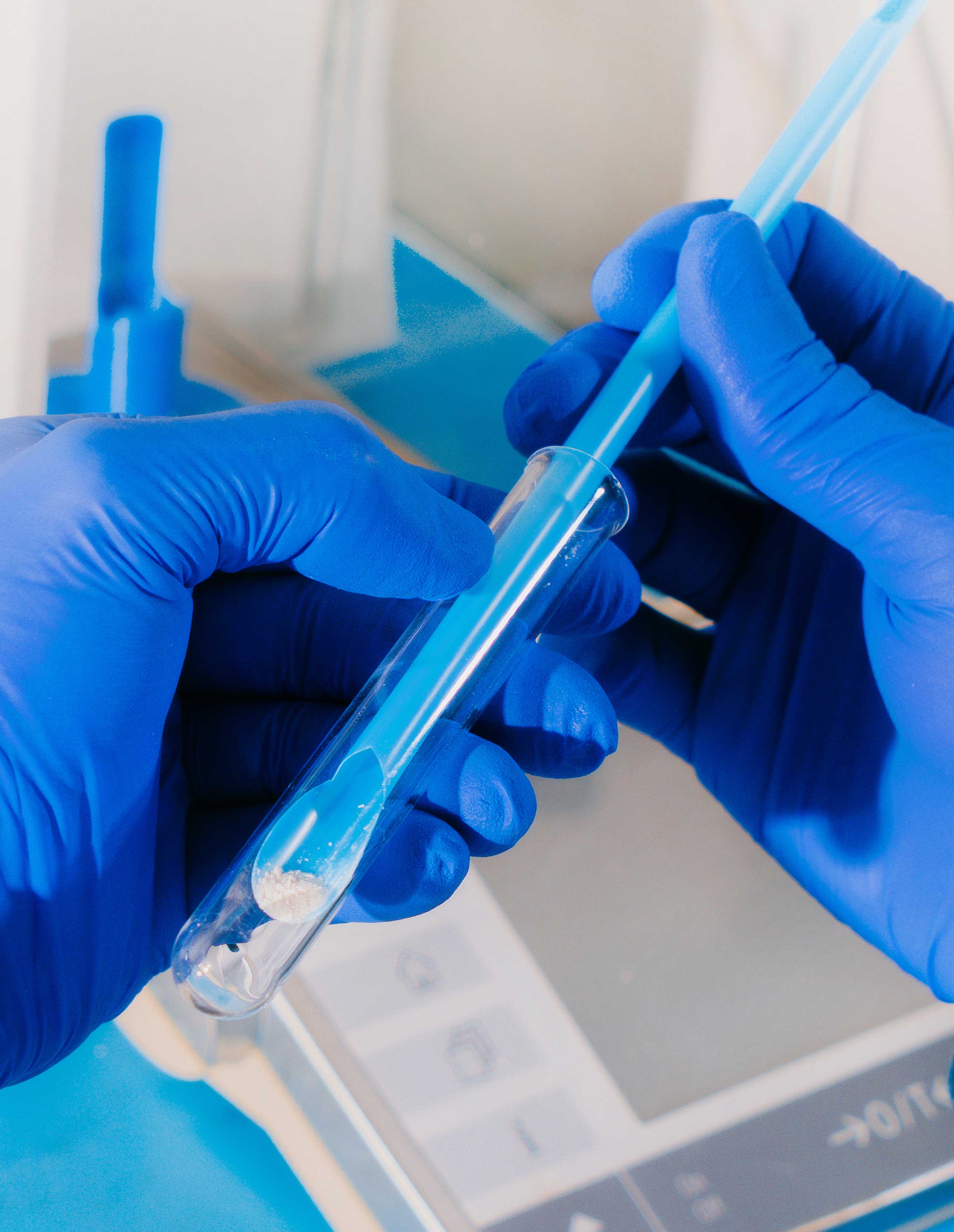 A lab technician’s gloved hands place a long spoon into a specimen bag with a crushed pill.