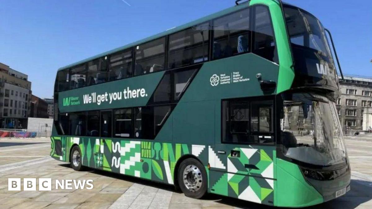 A green, black and white double decker bus parked in a square on a sunny day.