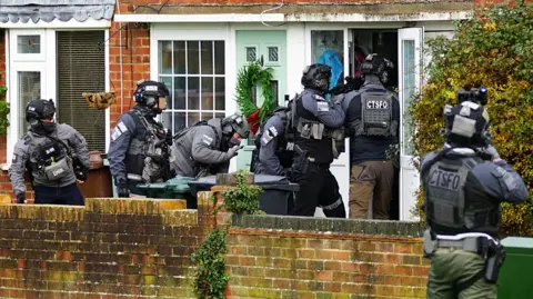 Dan Jessup Multiple police officers in body armour entering a door. some are carrying rifles. CTSFO can e read on some of their flak jackets.