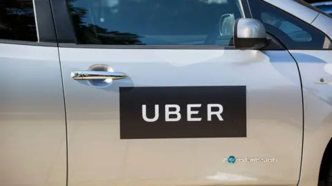 Laura Dale/PA The side of a silver car with a black sign on the driver's door saying UBER in white letters against a black rectangle. There is a small embossed sign below saying Zero emission.