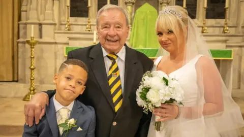 Carley James Dion wears a blue suit and cream tie, his great grandfather a dark blazer and yellow striped tie and Carley is pictured in her white wedding dress inside a church. 