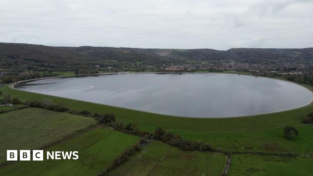 Aerial footage of Cheddar Reservoir, which has green fields in the foreground and the town in the background.
