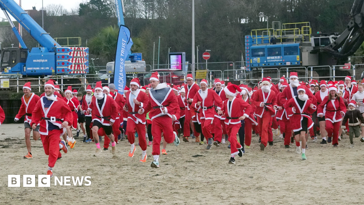 Dozens of runners dressed up like Santas running on Weymouth beach as part of the Chase the Pudding event. It's an overcast day.