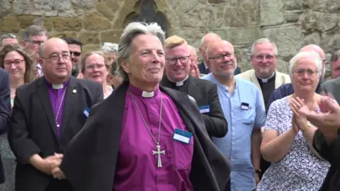 Archbishop of Wales Cherry Vann smiling in front of other members of the clergy and lay members, who are applauding her, following her election last July at an electoral college in Monmouthshire