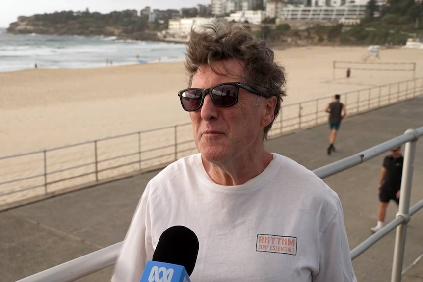 a man wearing sunglasses talking to a reporter on the promenade at bondi beach