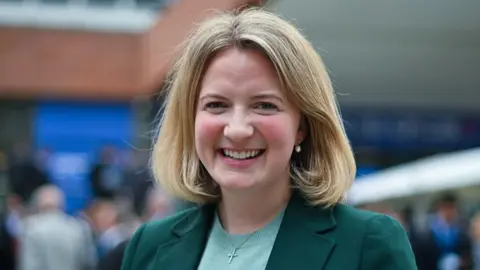 Getty Images A photograph on the MP Katie Lam smiling. She is wearing a green blazer. 