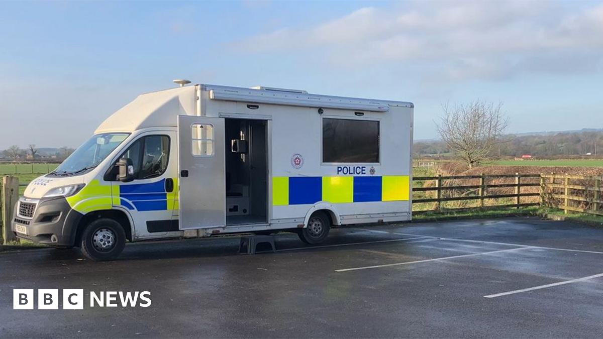 A large police lorry with the side door open on a car park by a field
