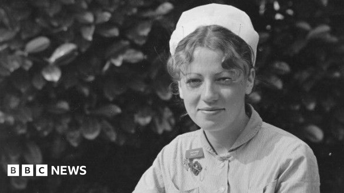 A black and white photo taken of Ann Remmers as a young midwife. She is wearing hospital scrubs and a white cap.  Her curly hair is pulled back and tucked underneath her cap, with a few pieces pulled out at the front.