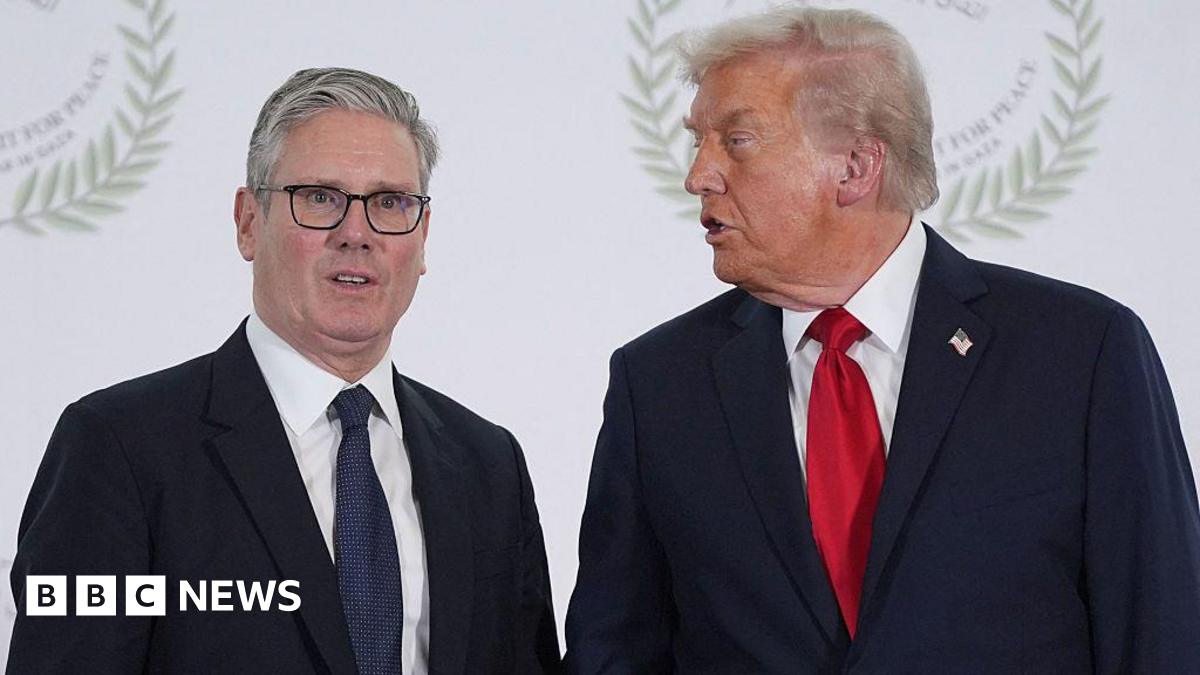 Sir Keir Starmer stands beside US President Donald Trump at an event, both wearing dark suits and ties, with Trump turned toward Starmer as if speaking while Starmer looks toward the camera.