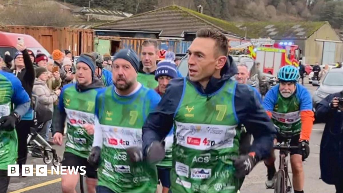 Kevin Sinfield with runners and people on bikes. He's wearing a green vest with sponsorship and a big number 7. It looks very cold.