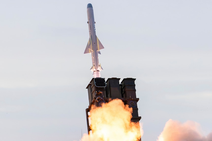 a white missile with triangular fins is launched from a cartridge with orange flames coming out.
