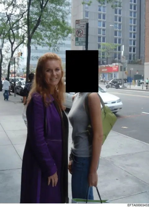 US Department of Justice Sarah Ferguson, wearing a purple coat, standing next to a woman on the street whose face is redacted. The woman is wearing a grey tank top and has a green shoulder bag.
