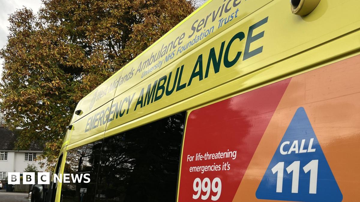 A close-up shot of the side of an ambulance. At the top it says West Midlands Ambulance Service University NHS Foundation Trust. Below that in larger lettering it says emergency ambulance, and at the bottom in white lettering against a red background it says for life-threatening emergencies it's 999