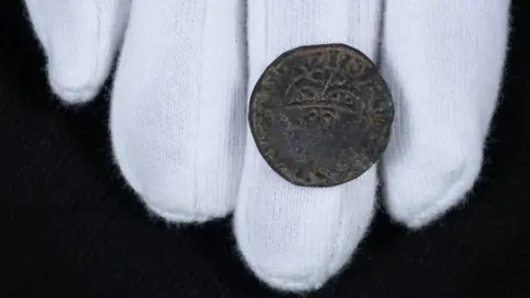 PA Media A coin rested on a white gloved hand. The close up image was taken against a black felt background.