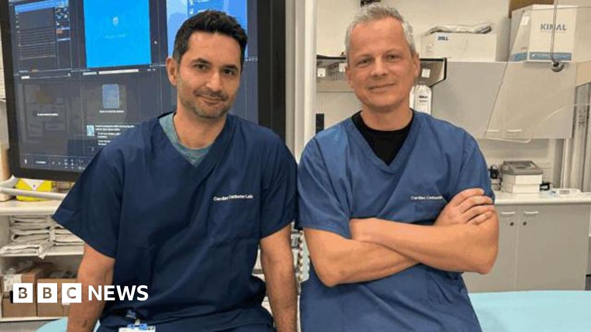 Two male doctors in scrubs looking at the camera. One man has dark stubble and short dark hair, and the other has short white hair.