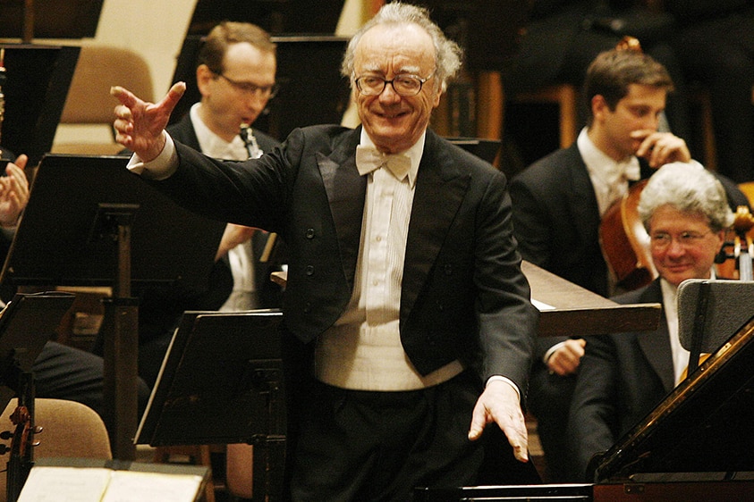 Pianist Alfred Brendel stands front of an orchestra, smiling after taking a bow.