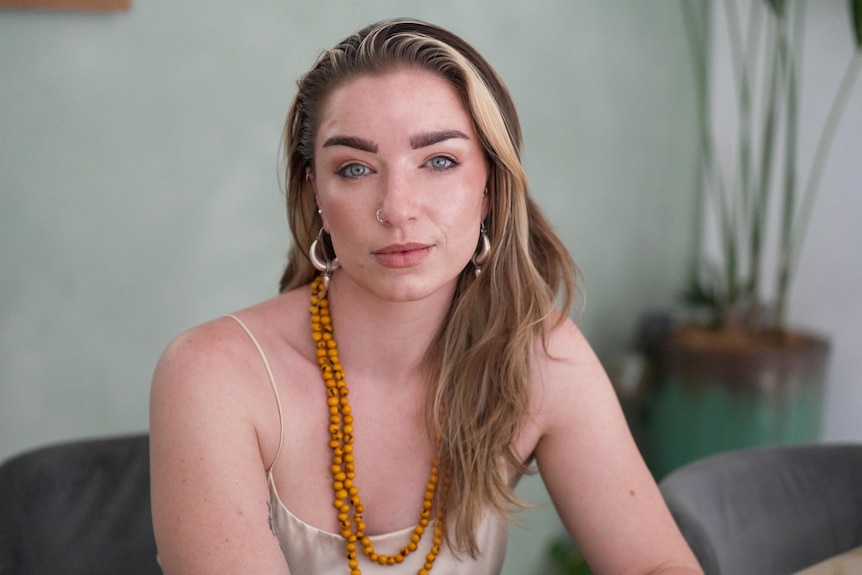 A woman with dark blonde hair and an orange necklace and earrings staring at the camera.