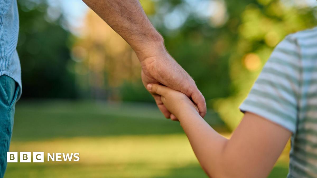 A man holding a child's hand standing in a park