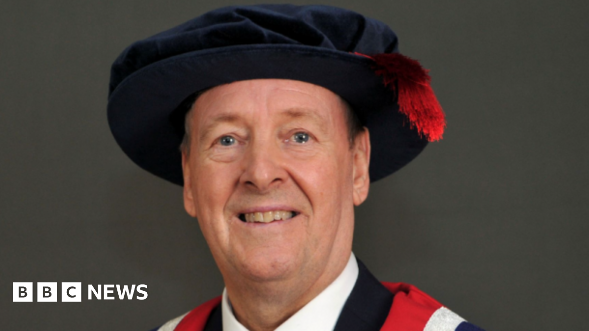 Nick Broady wearing a graduation cap and gown after receiving his honorary fellowship for his commitment to charity. He is smiling into the camera.