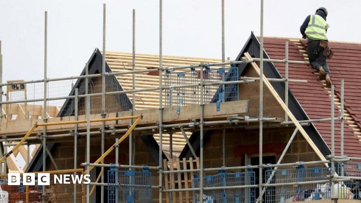 A man on a roof of a new home that is being built with scaffolding around it