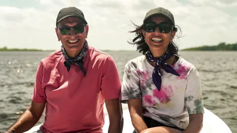 StudioLambert/BBC Anita Rani and dad Bal smiling whilst on a boat wearing matching navy neckerchiefs.