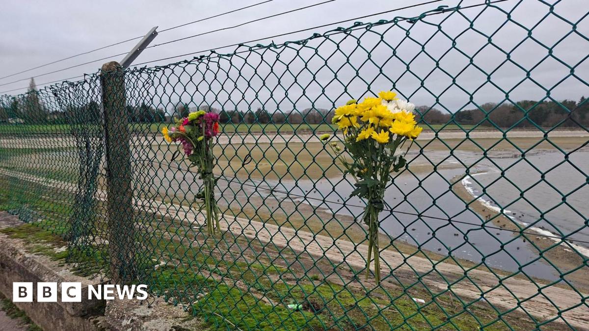 Two floral tributes left on a fence outside of a reservoir. The flowers are a mixture of colours.