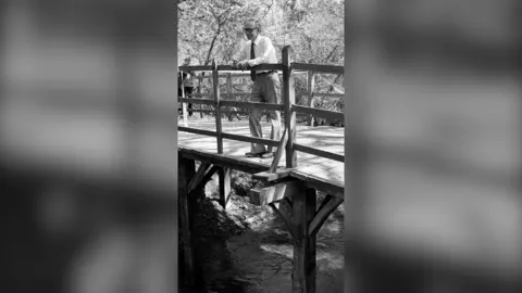 PA Media Black and white image of elderly Christopher Milne on the original Pooh Bridge in Hartfield in 1979