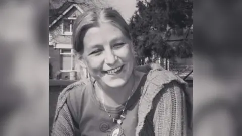 Handout Black and white image of Dawn Sturgess smiling. Her hair is tied back and she is wearing a loose cardigan.