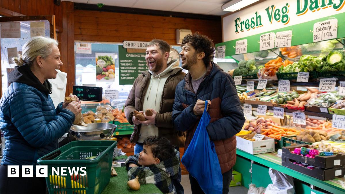 Two men and a young boy buying fruit and veg in a greengrocers.