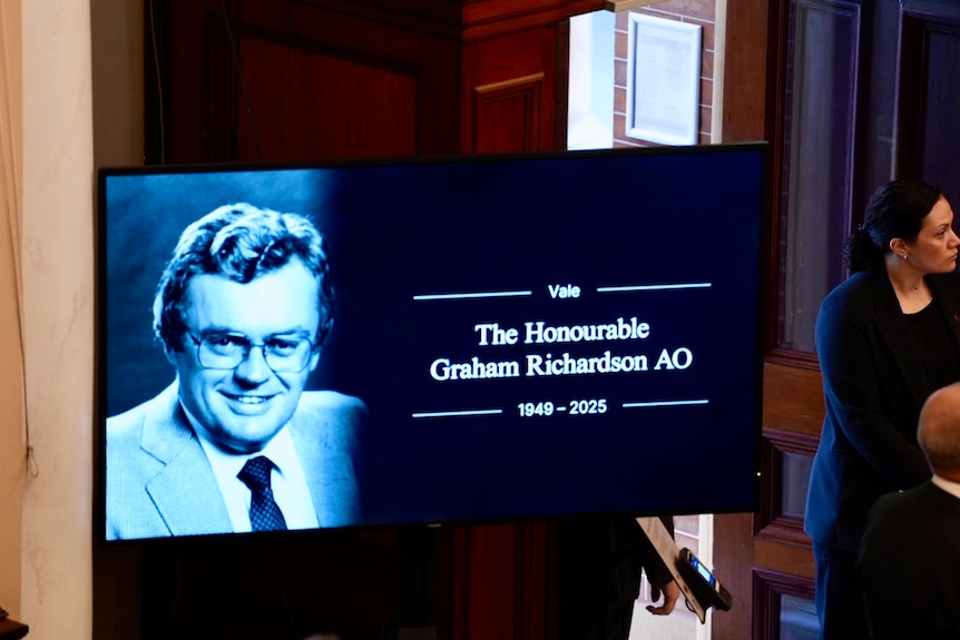 A TV screen showing an old photo of Graham Richardson