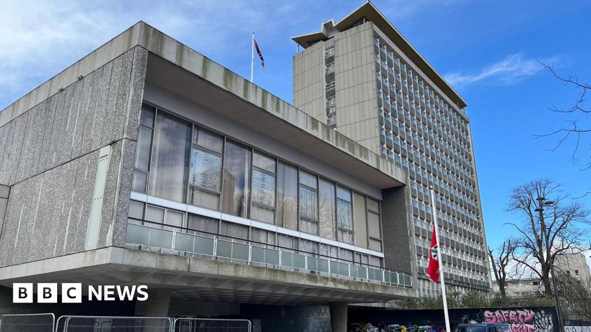 The concrete and glass building of the Civic Centre in Plymouth with the Civic Centre tower block to the right, Plymouth's flag is hanging from a flagpost at the front of the building.