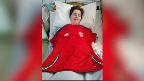 Family handout Kyle Sieniawski, pictured lying in a hospital bed with a Wales football jersey laid across his body, with signatures on it.