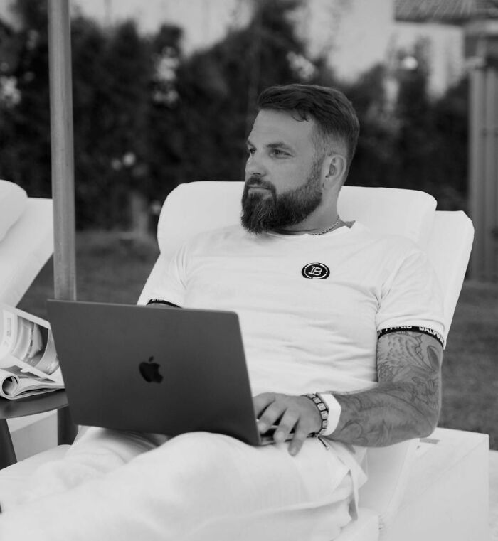 Man with beard and tattoos using a laptop outdoors, related to crypto scammer case in Dubai mall investigation.